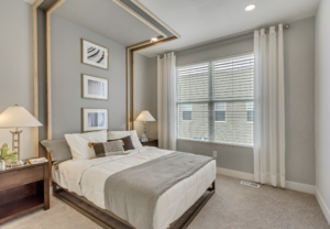 Modern bedroom with a neatly made bed, decorative pillows, bedside lamps, and framed art on a gray wall.